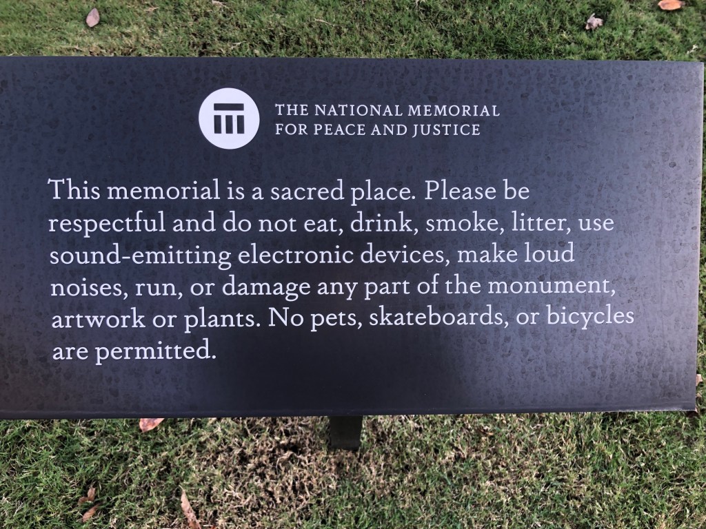 Sign at The National Memorial for Peace and Justice that reads: This memorial is a sacred place. Please be respectful and do not eat, drink, smoke, litter, use sound-emitting electronic devices, make loud noises, run, or damage any part of the monument, artwork, or plants. No pets, skateboards, or bicycles are permitted.