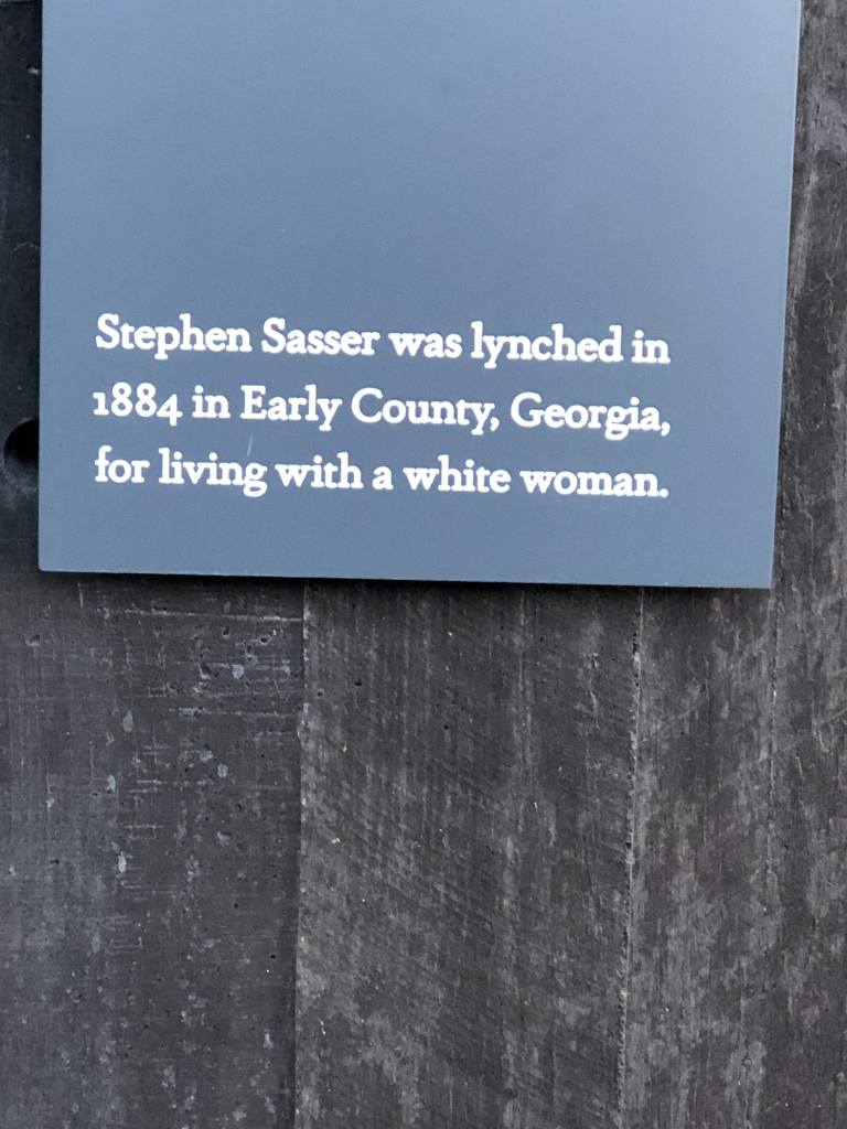 Grey sign mounted on a dark wood board reads: Stephen Sasser was lynched in 1884 in Early County, Georgia, For living with a white woman.